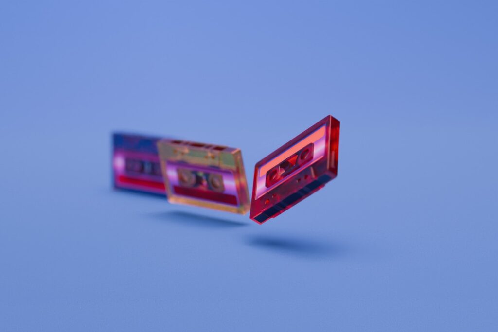 Retro audio cassette tapes rendered in glossy translucent plastic appear suspended or aligned in space over a seamless blue backdrop, highlighting form, vibrant color and nostalgic technology.